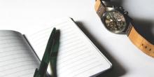 Image of pen laying on notebook with a watch next to notebook