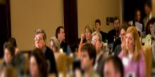 Audience sitting down in an auditorium listening to speaker on stage. 